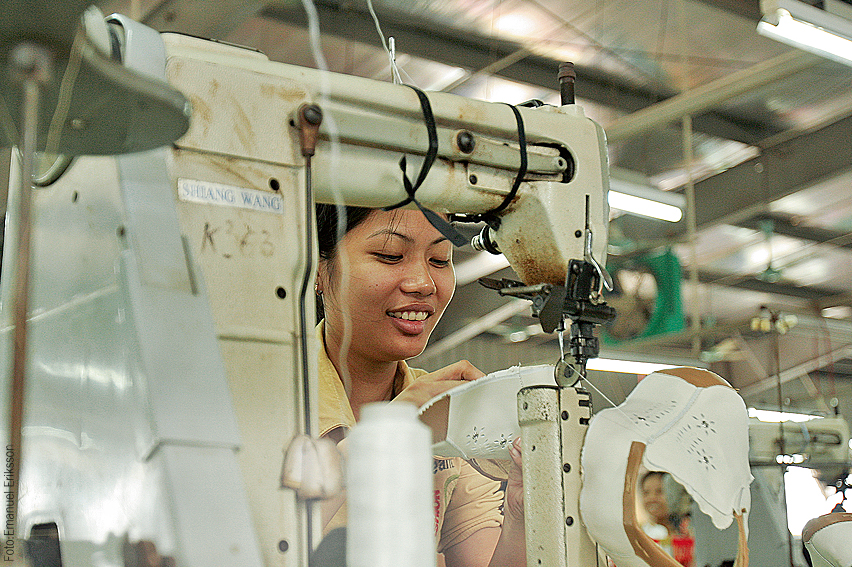 Kvinna arbetar vid symaskin i asiatisk fabrik